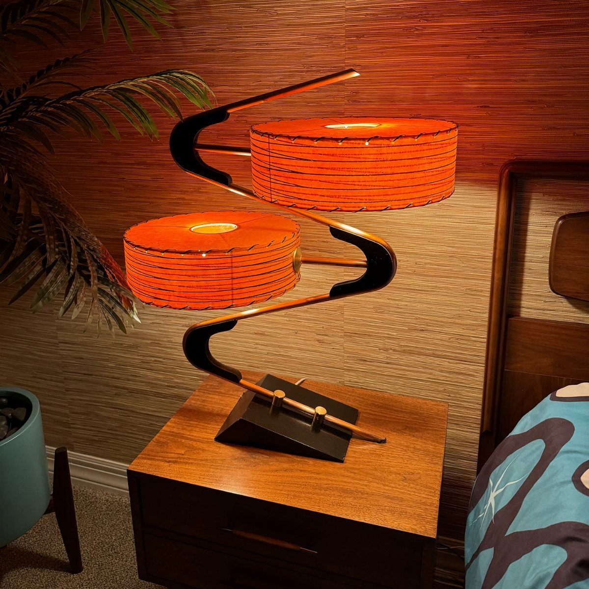 Sculptural orange lamp with winding base on a wooden mid-century modern nightstand.