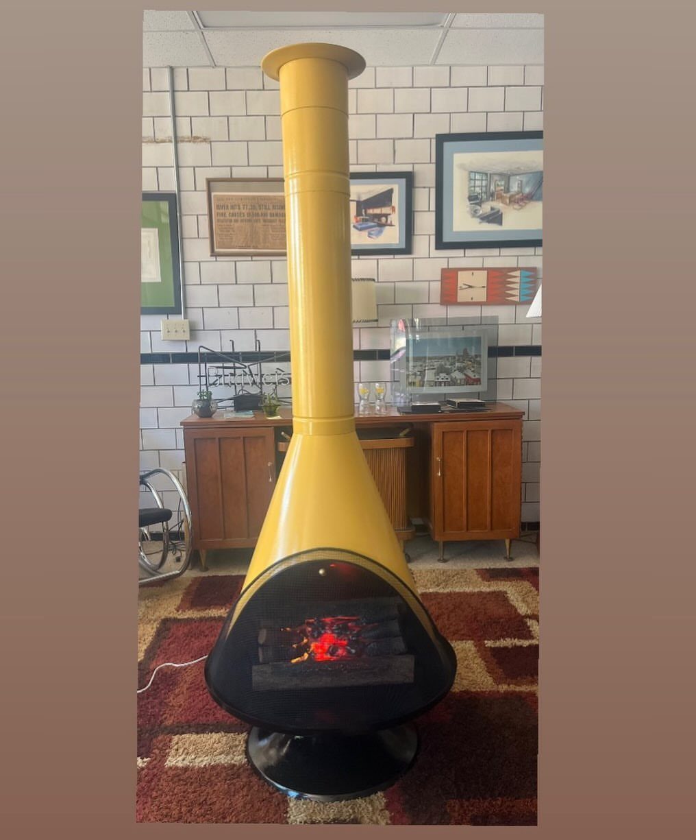Yellow conical freestanding fireplace with a tall chimney on a brown patterned rug.