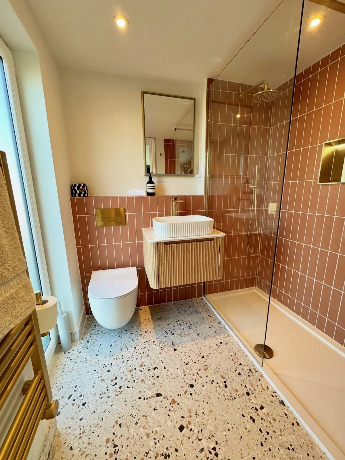 Terrazzo floor tiles in a modern bathroom with terracotta walls and glass shower.