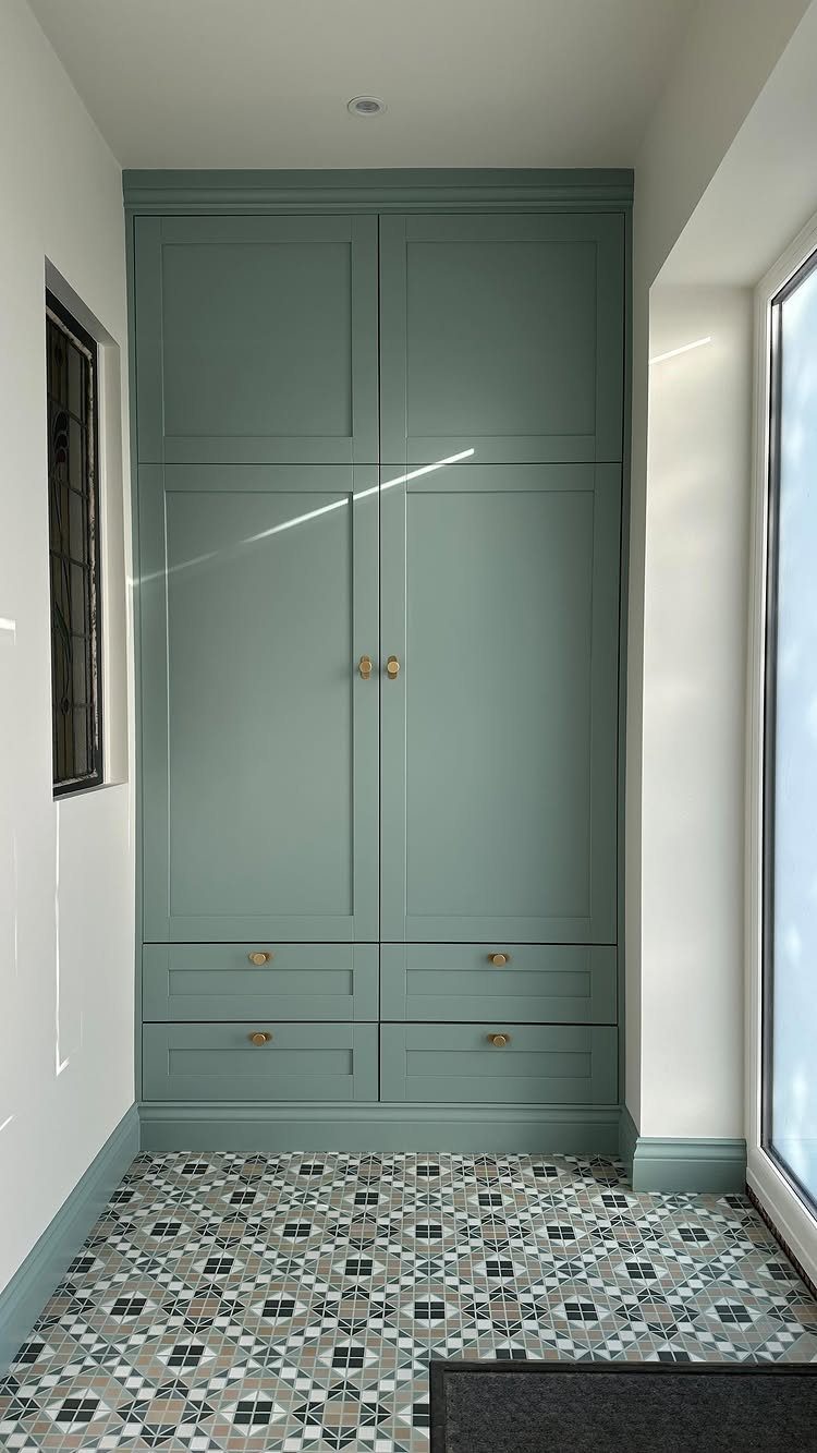 Sage green built-in wardrobe with gold hardware and patterned floor tiles in hallway.