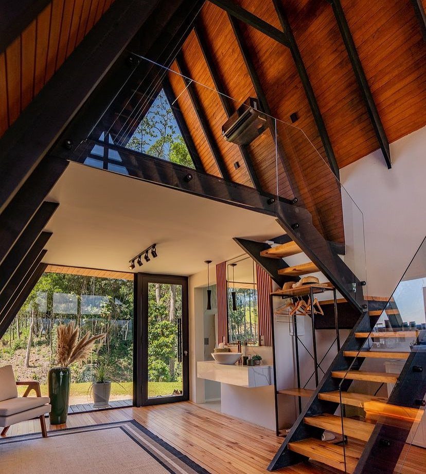Modern A-frame home interior with vaulted wooden ceilings, steel beams, and forest views.