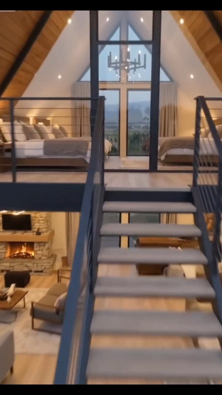 Modern A-frame home interior with a loft bedroom and stone fireplace living area.