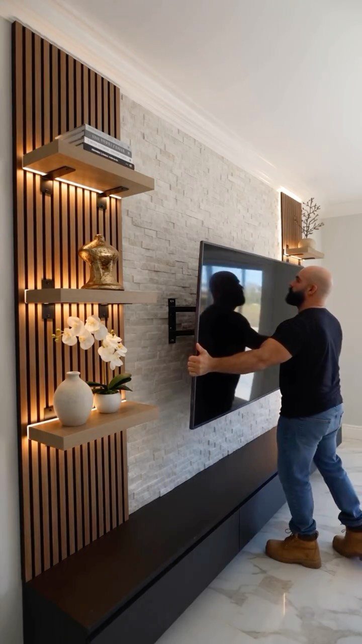 Man mounting a TV on a white stone accent wall with wood slats.