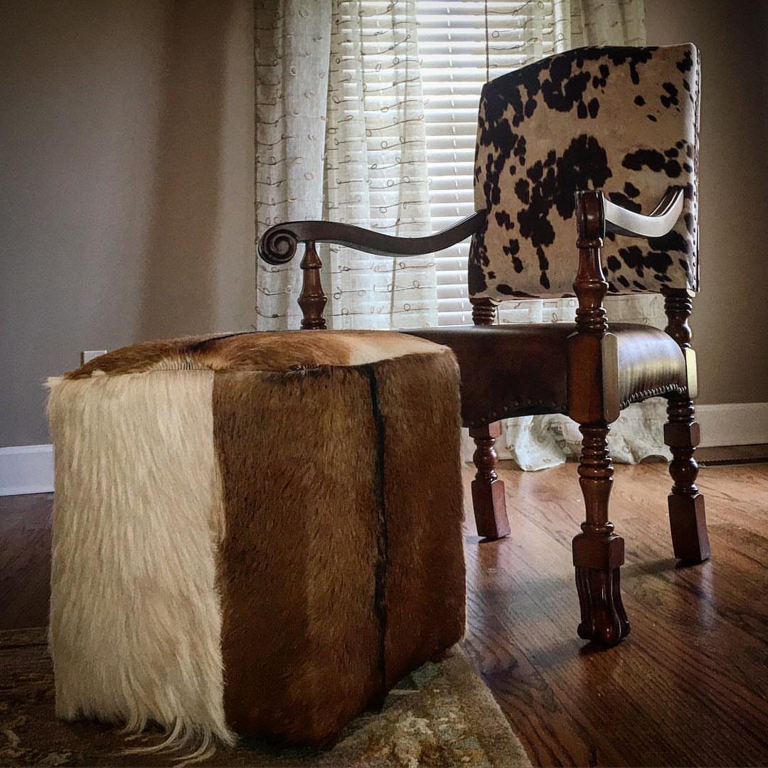 Cow-print upholstered wooden armchair and matching cowhide ottoman on a wooden floor.