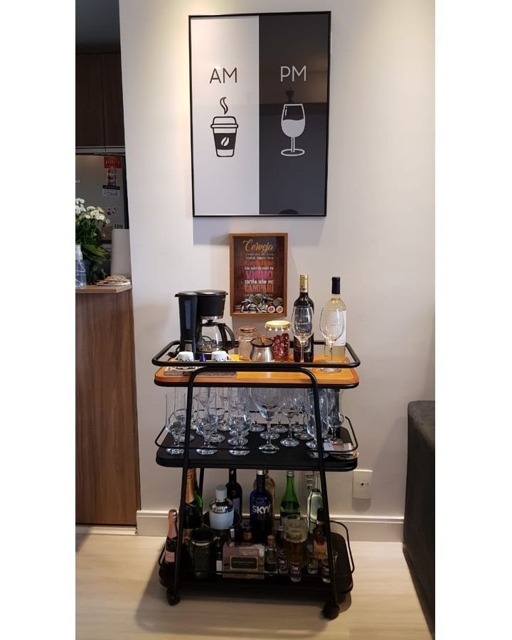 Three-tier black metal bar cart stocked with liquor and glassware against a white wall.