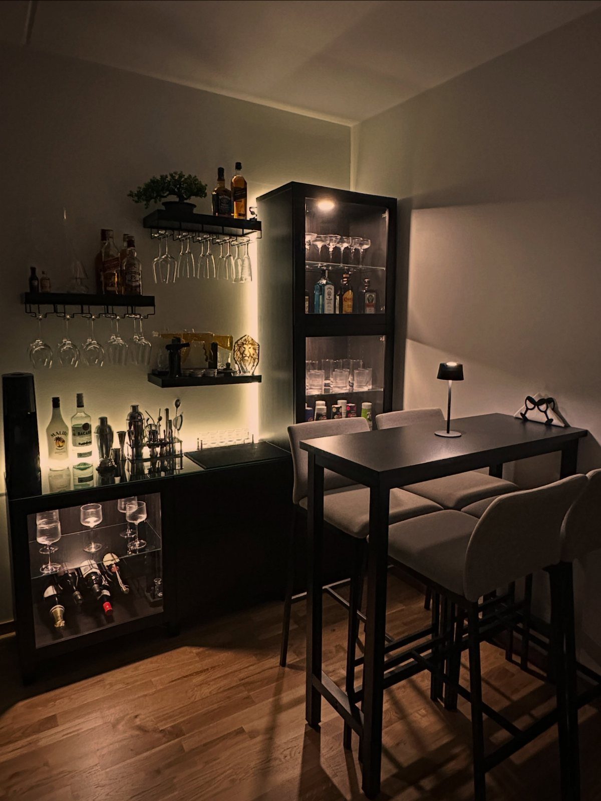 Modern home bar setup with black cabinets, liquor bottles, and grey bar stools.