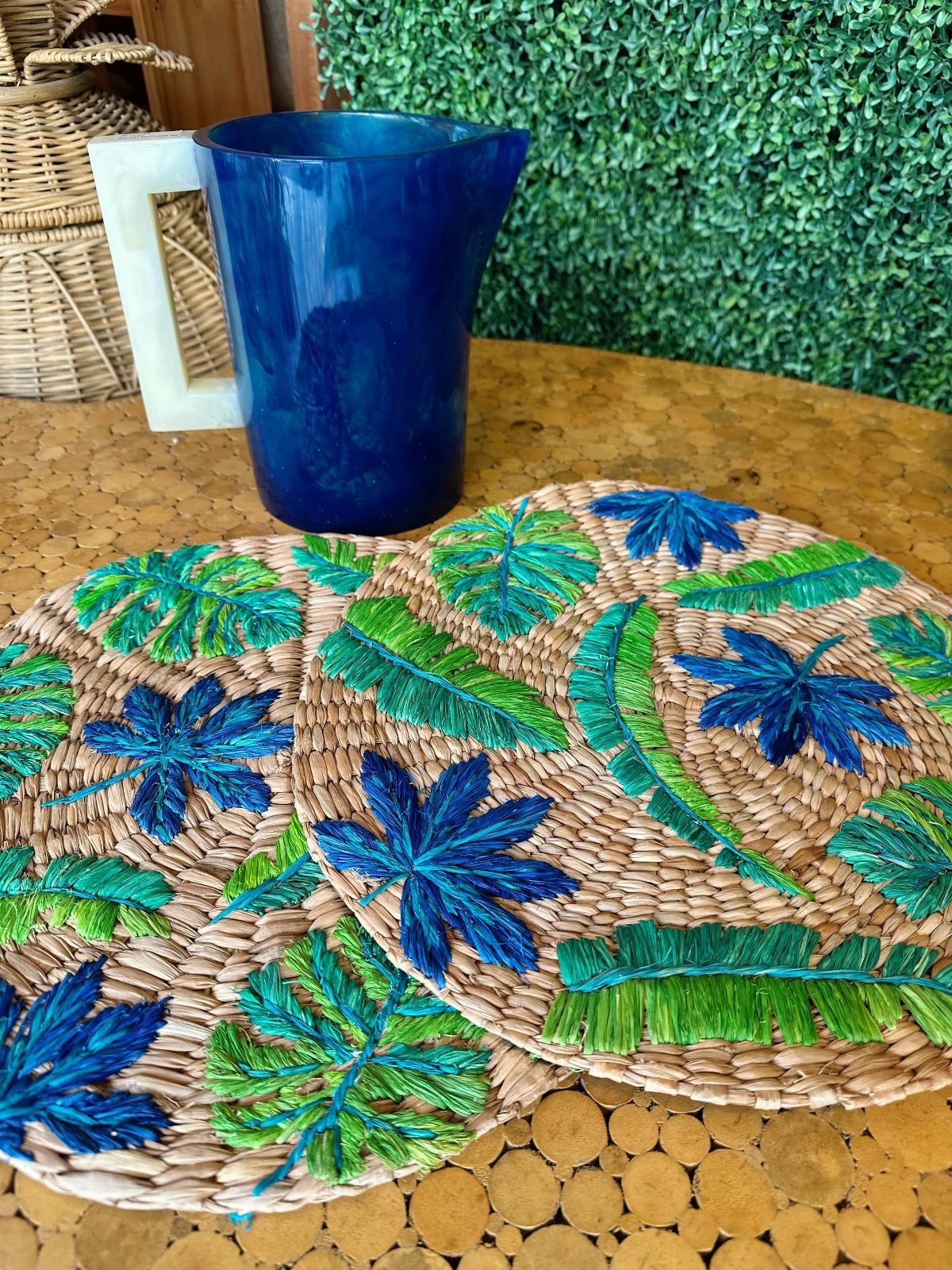 Blue glass pitcher and woven tropical leaf placemats on a gold textured surface