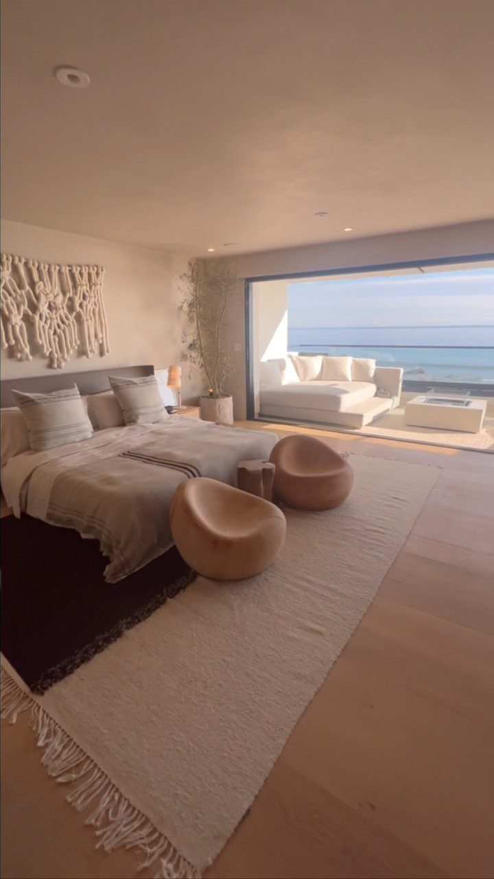 Modern coastal bedroom with neutral linens and open doors overlooking the ocean.