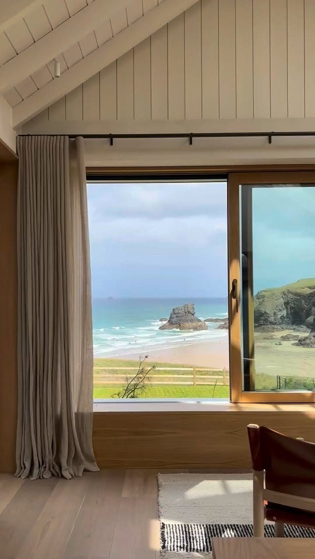 Large wooden window overlooking a sandy beach and ocean in a bright room
