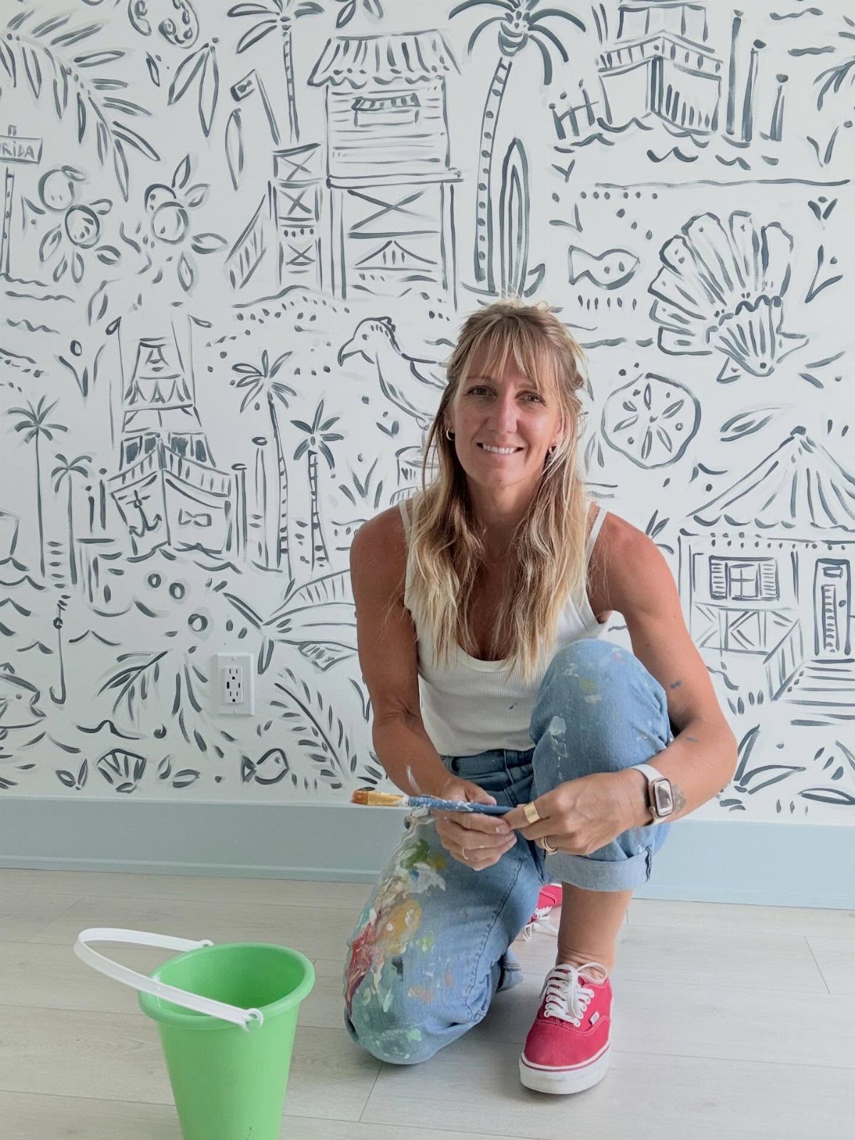 Woman posing in front of a blue line coastal mural on a white wall