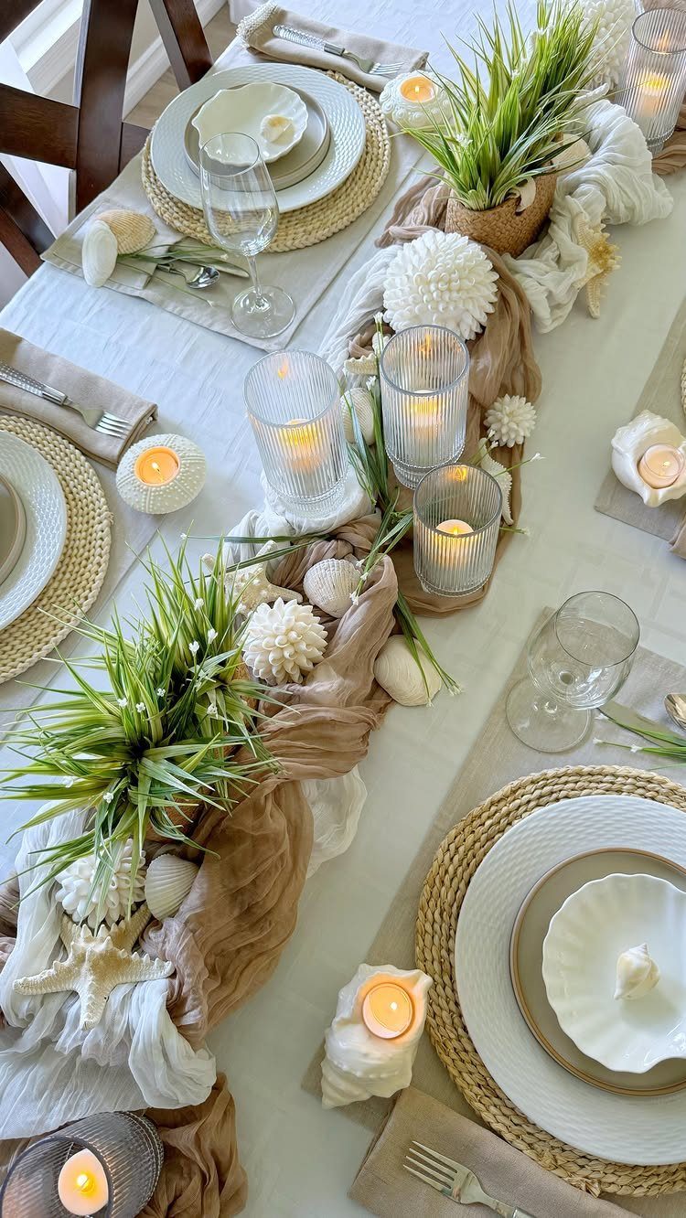Coastal dining table setting with woven placemats, seashells, and green plants.