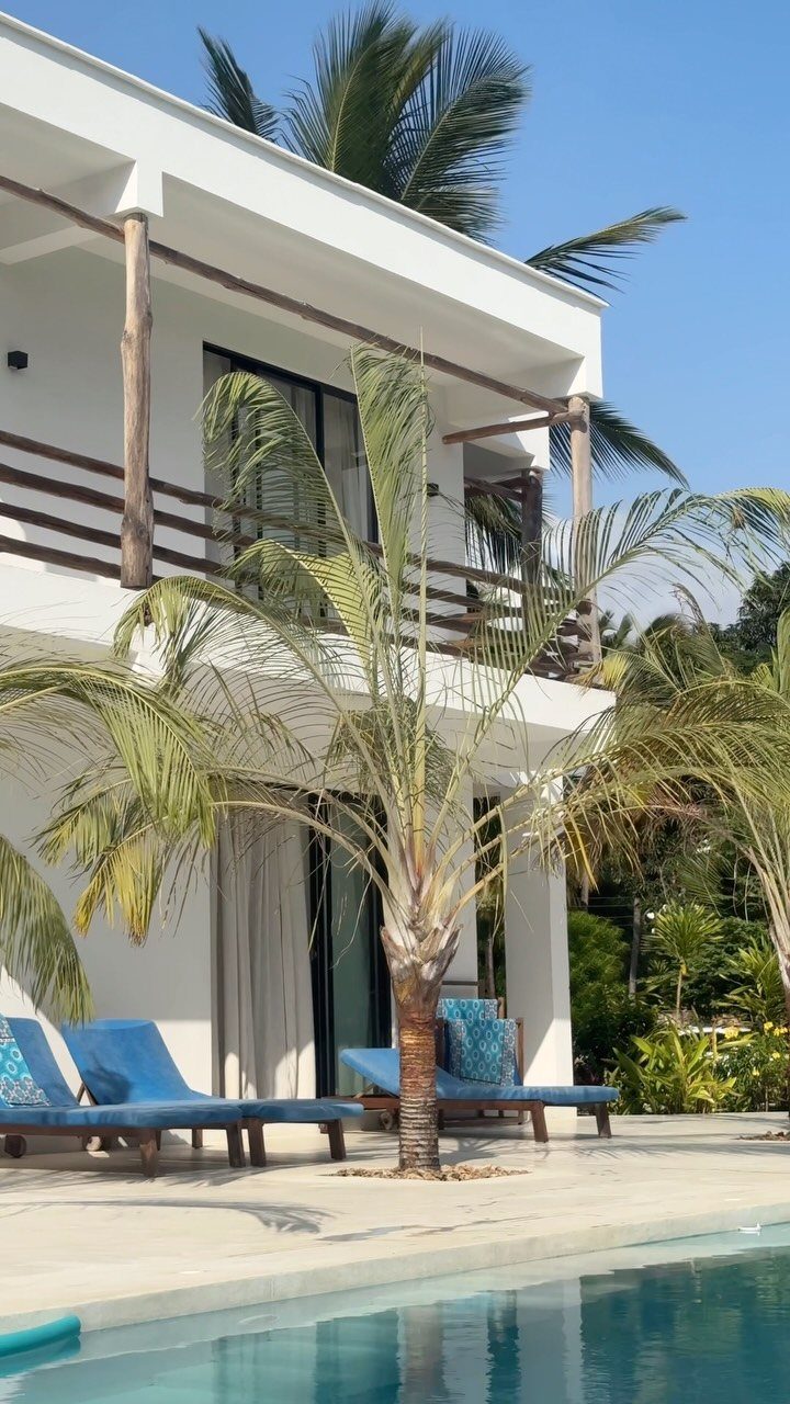 White beach house with wooden balconies, blue lounge chairs, and a swimming pool.