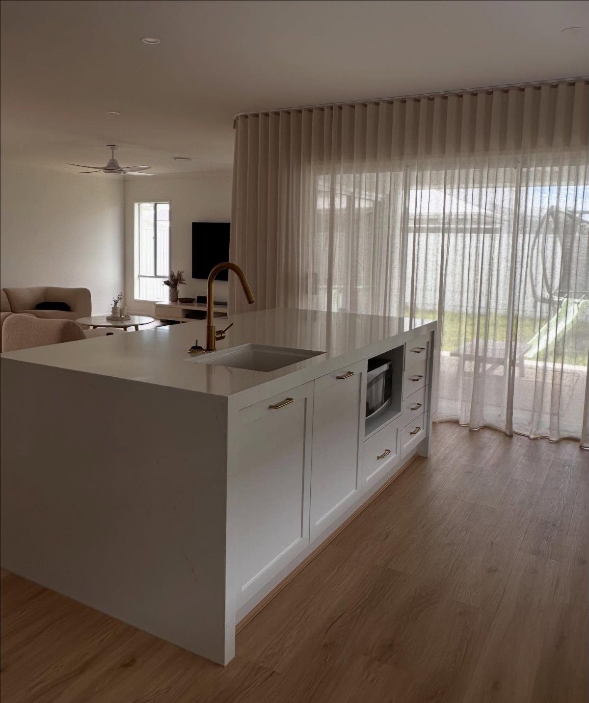 White kitchen island and light wood floors with sheer white drapes over glass doors
