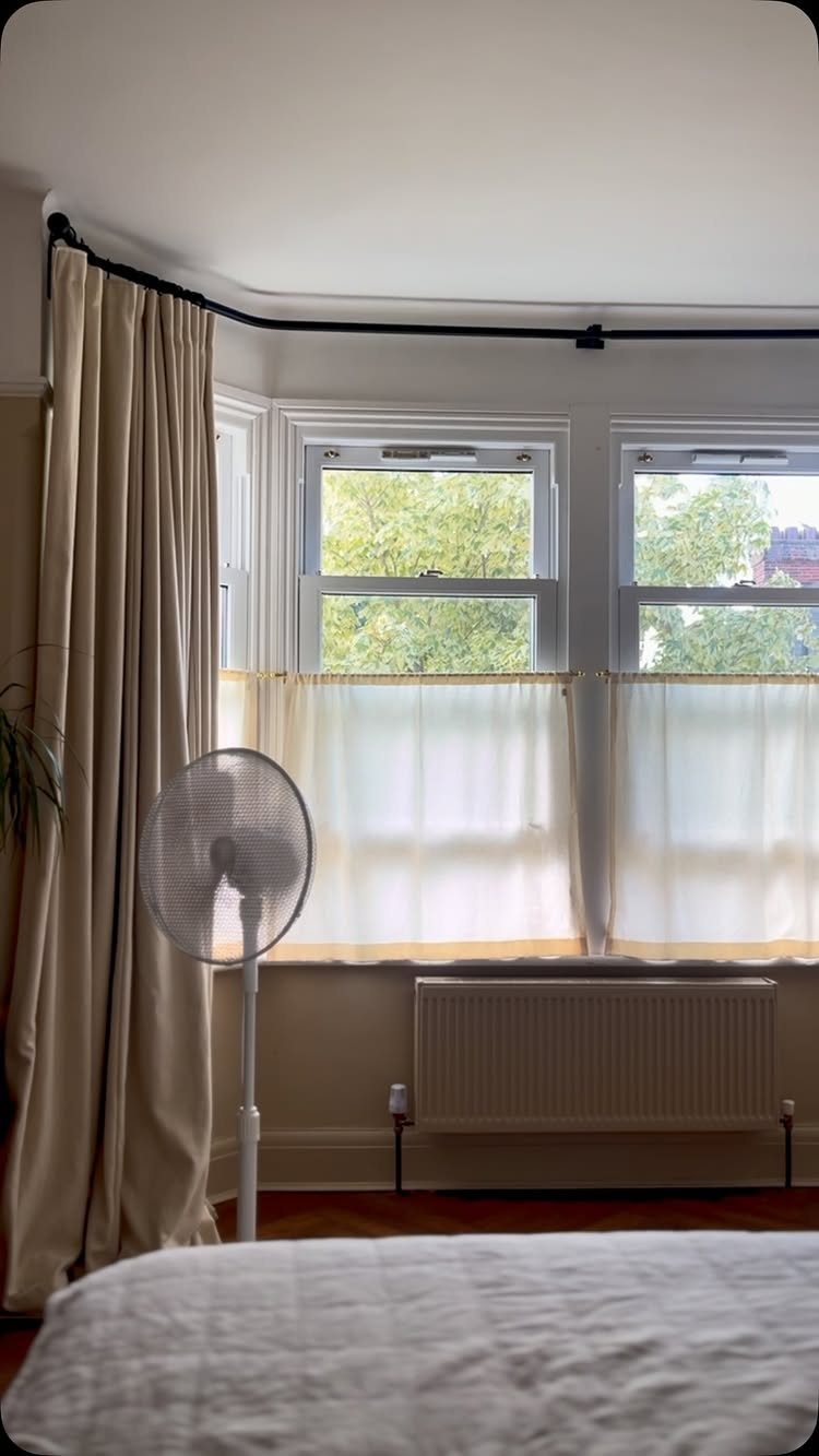 Cream curtains and sheer cafe curtains framing large bay windows in a bedroom