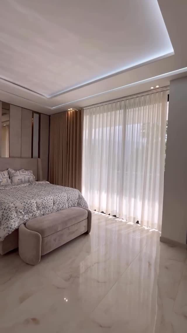 Floor-to-ceiling white sheer and beige curtains in a modern bedroom with marble floors.