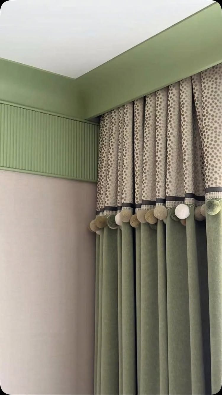 Green velvet curtains with patterned top and pom-pom trim in a modern room