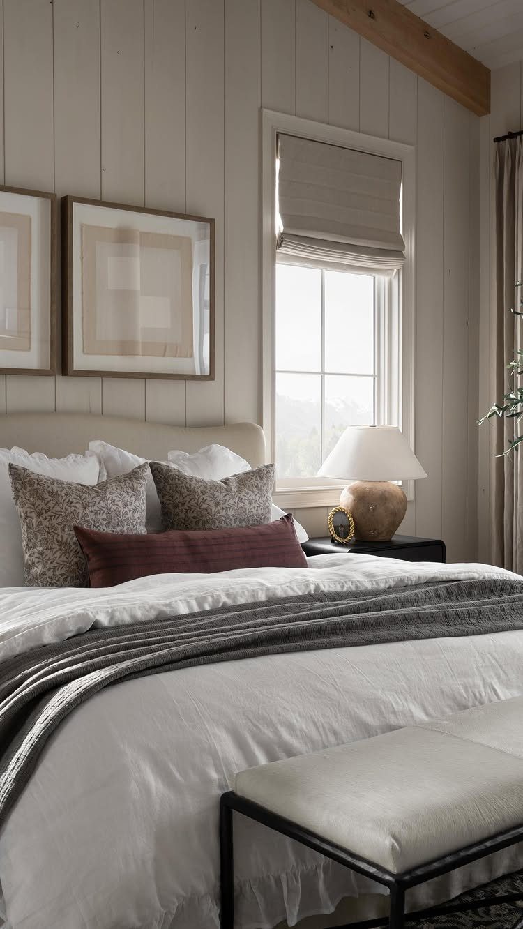 Beige Roman shade on a bedroom window next to a white bed.