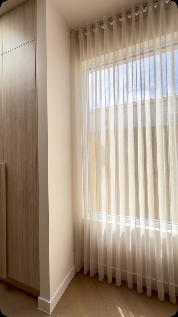 White sheer curtains covering a large window in a bright, modern room.
