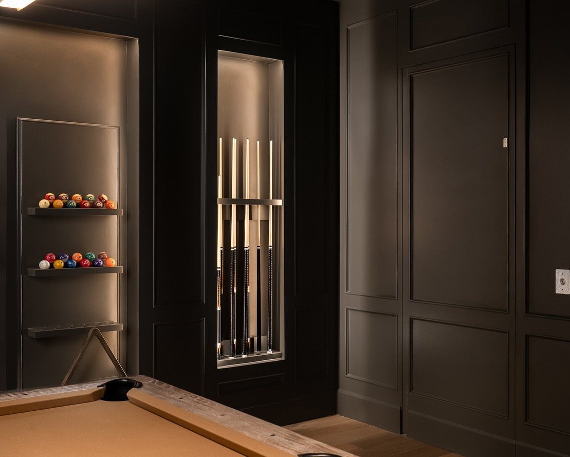 Billiard room with black paneled walls, pool cues in a niche, and colorful balls.