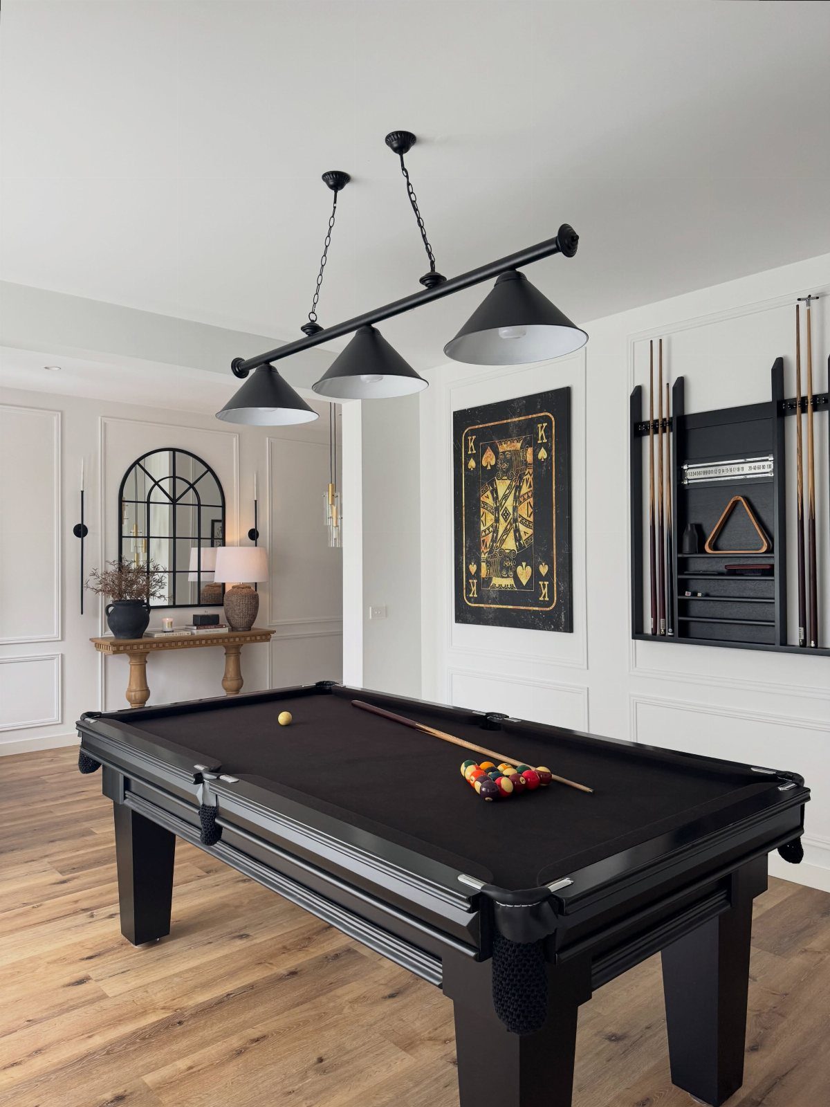 Black pool table with matching black lighting and cue rack on hardwood floors