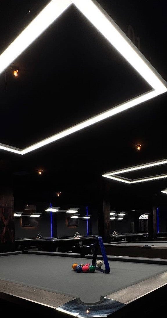 Billiard room with grey pool tables under large rectangular LED ceiling lights