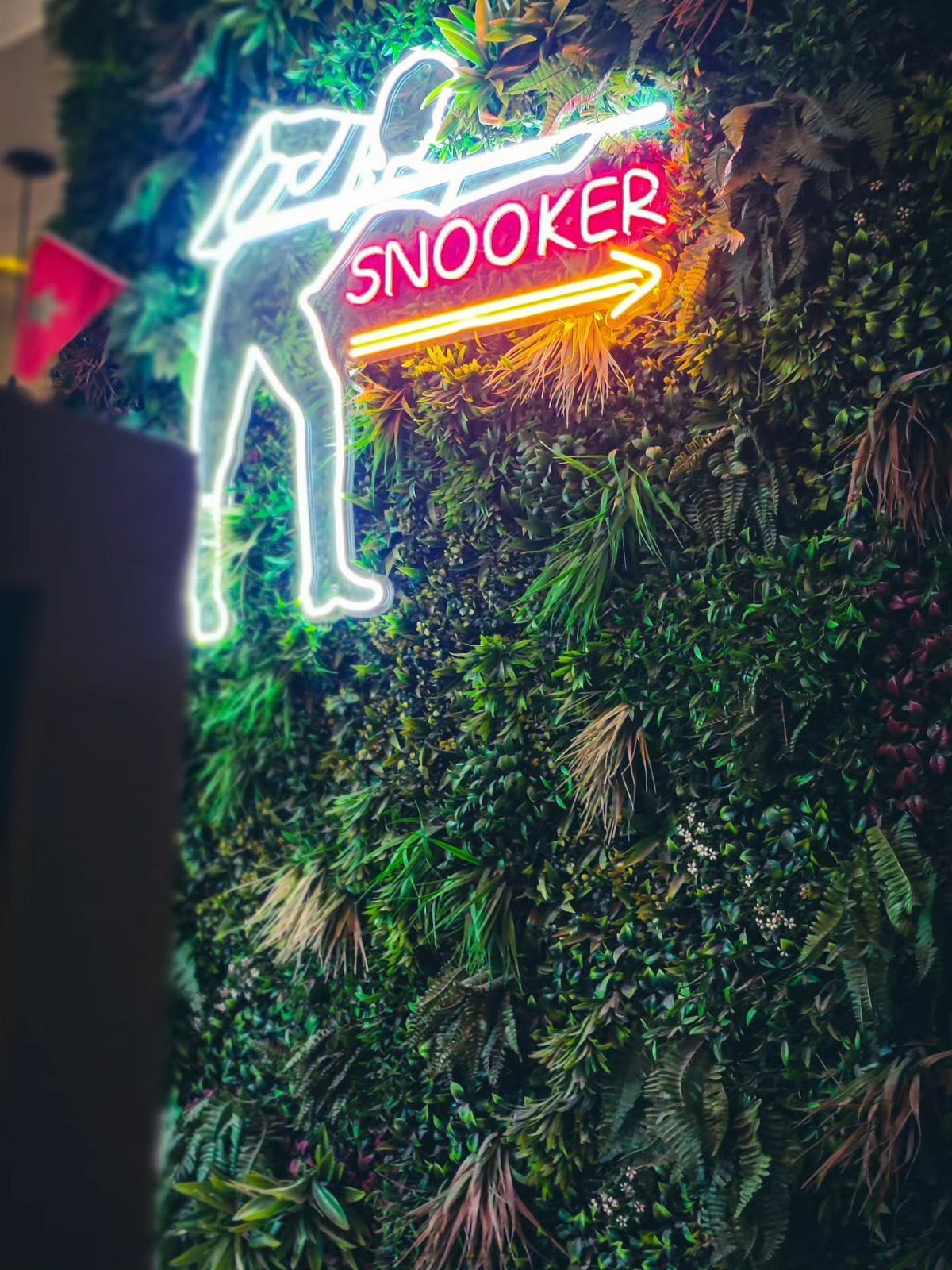 Neon snooker sign glowing against a lush green vertical plant wall