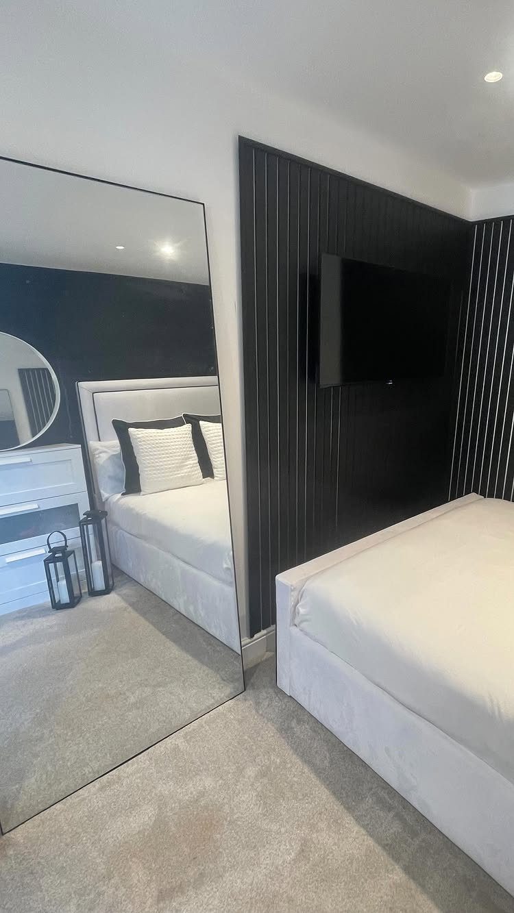 White bed with striped pillows in a bedroom with black slatted walls.