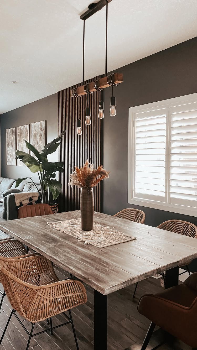 Dining room with dark grey walls, rustic wooden table, and woven rattan chairs.