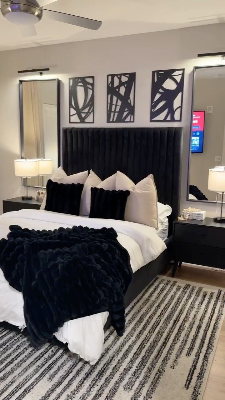 Bedroom with black velvet headboard, white bedding, black accents, and striped area rug.