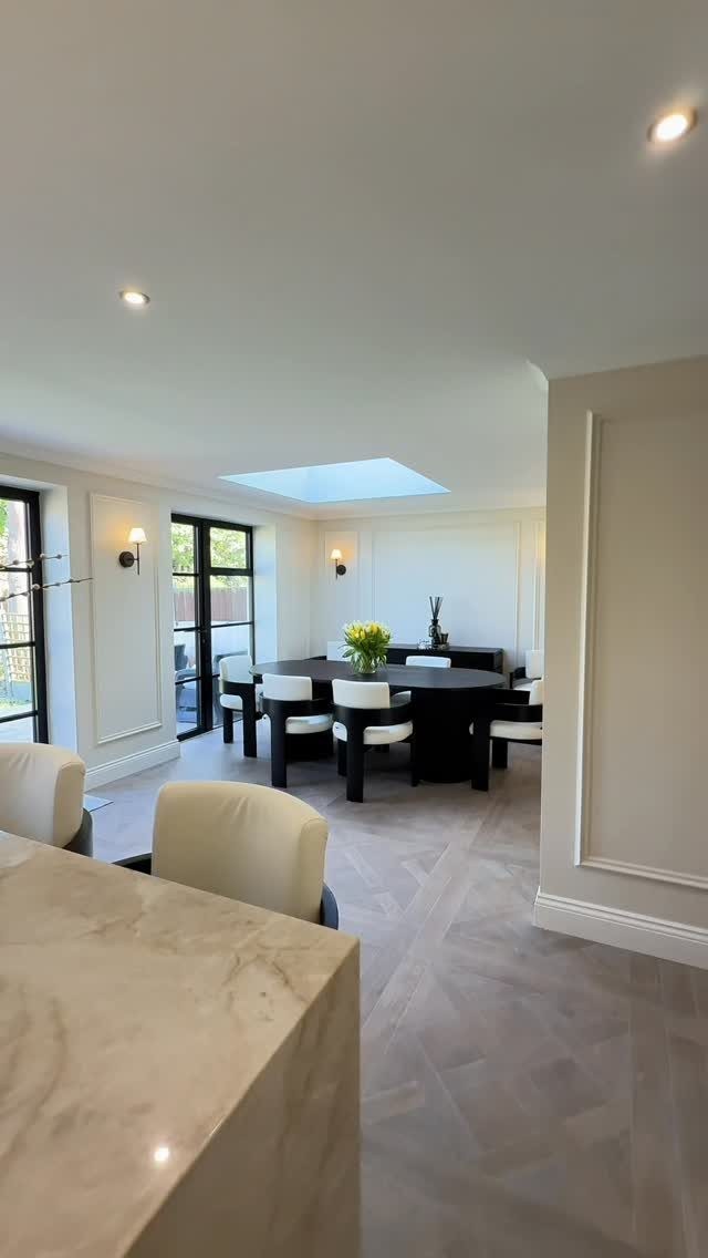 Black dining table with white chairs in a bright room with white walls.