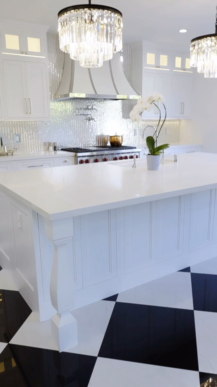 White kitchen with a black and white checkered tile floor and crystal chandeliers.