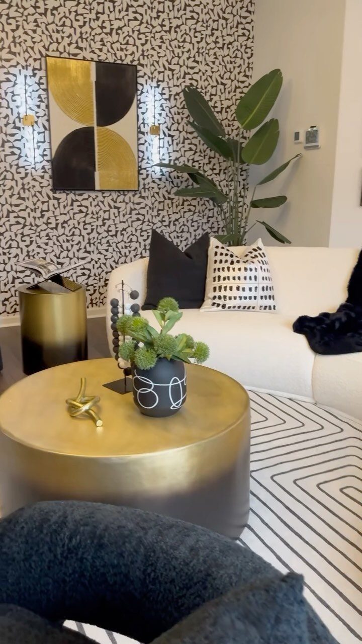 Modern living room with black and white patterned wallpaper and gold furniture accents.