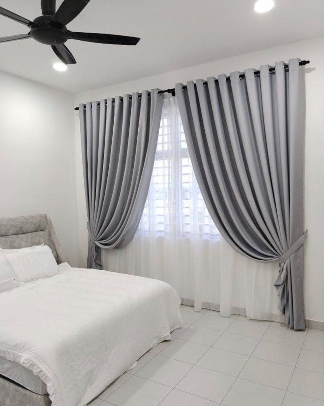 Grey curtains and white sheers layered over white horizontal blinds in a bedroom.