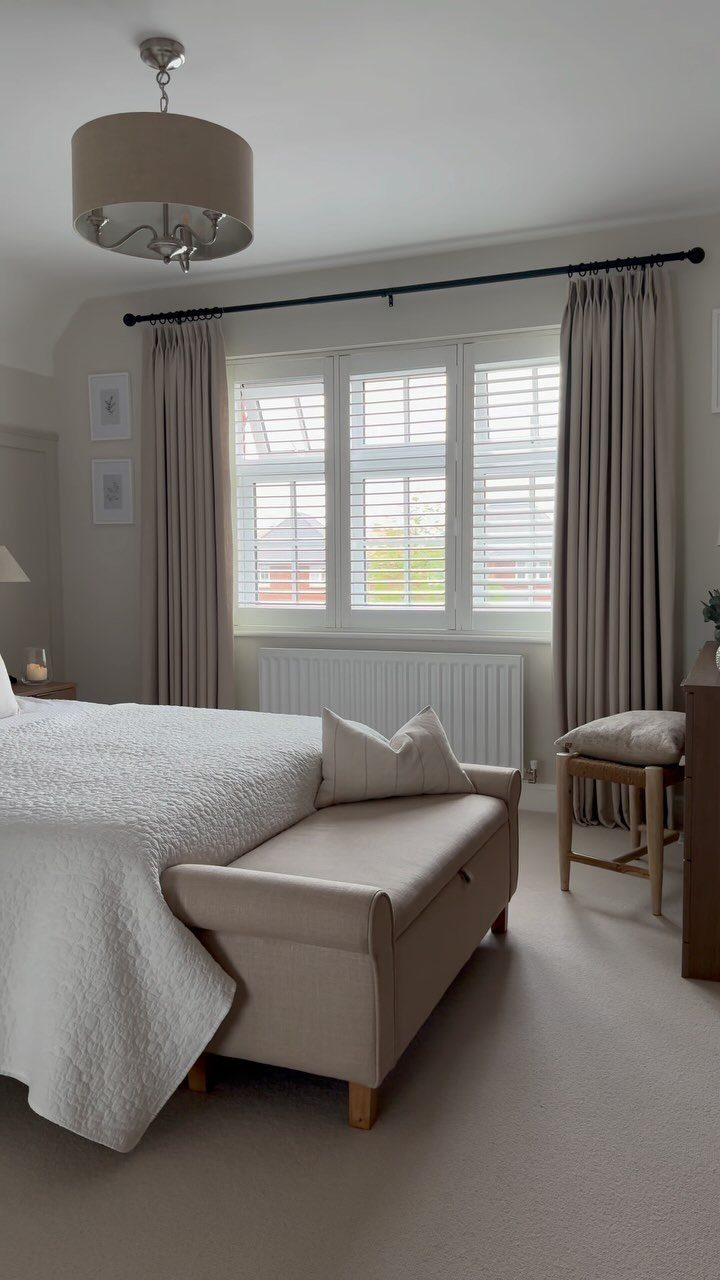 White plantation shutters paired with beige curtains in a neutral toned bedroom