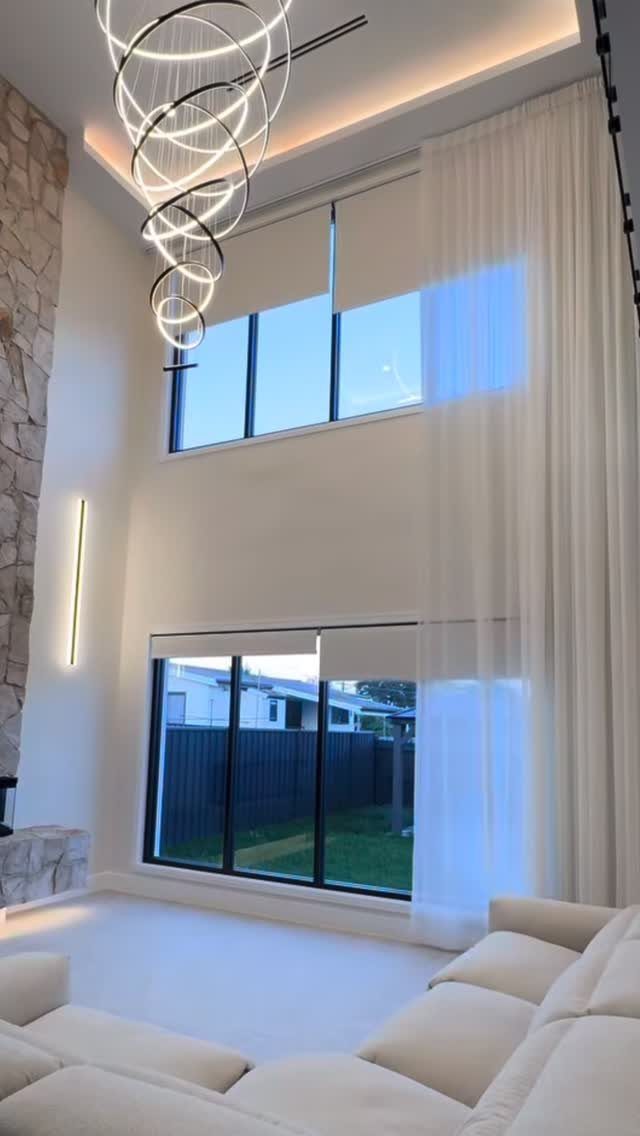 White sheer curtains and roller shades installed on large windows in a modern room.