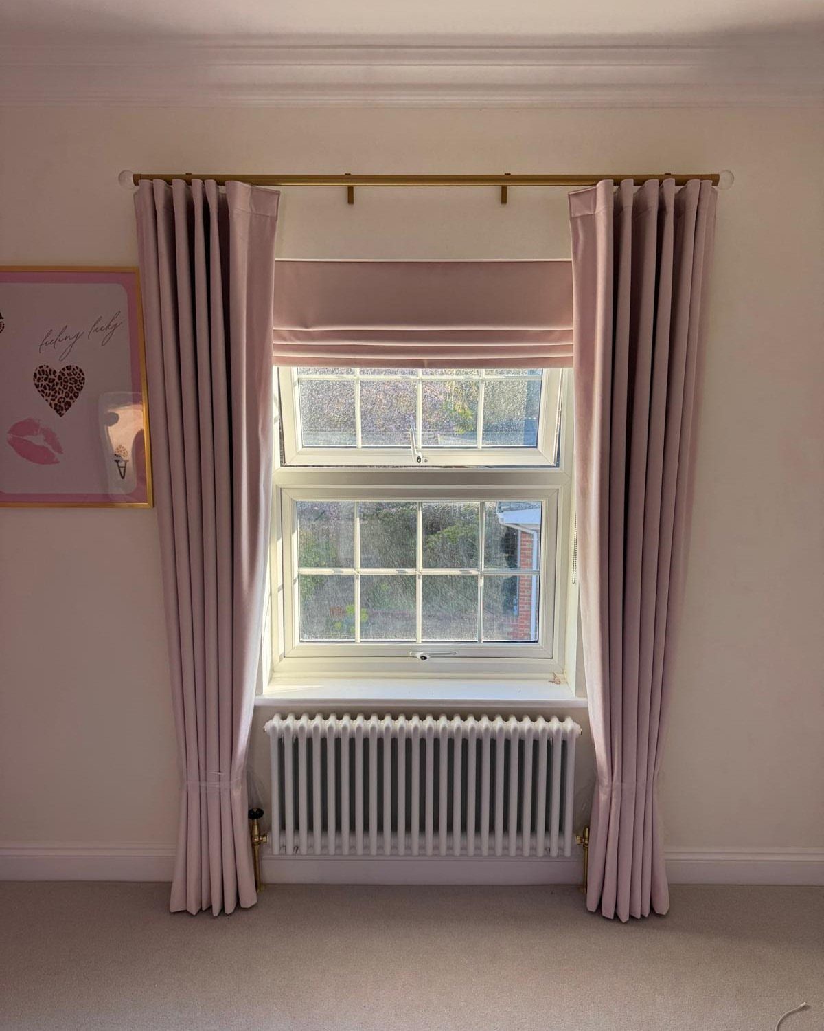 Light pink Roman blinds and matching curtains framing a white window and radiator.