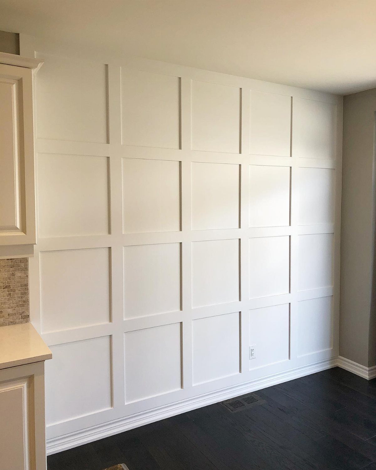 White grid board and batten wall with dark wood flooring and white cabinets.
