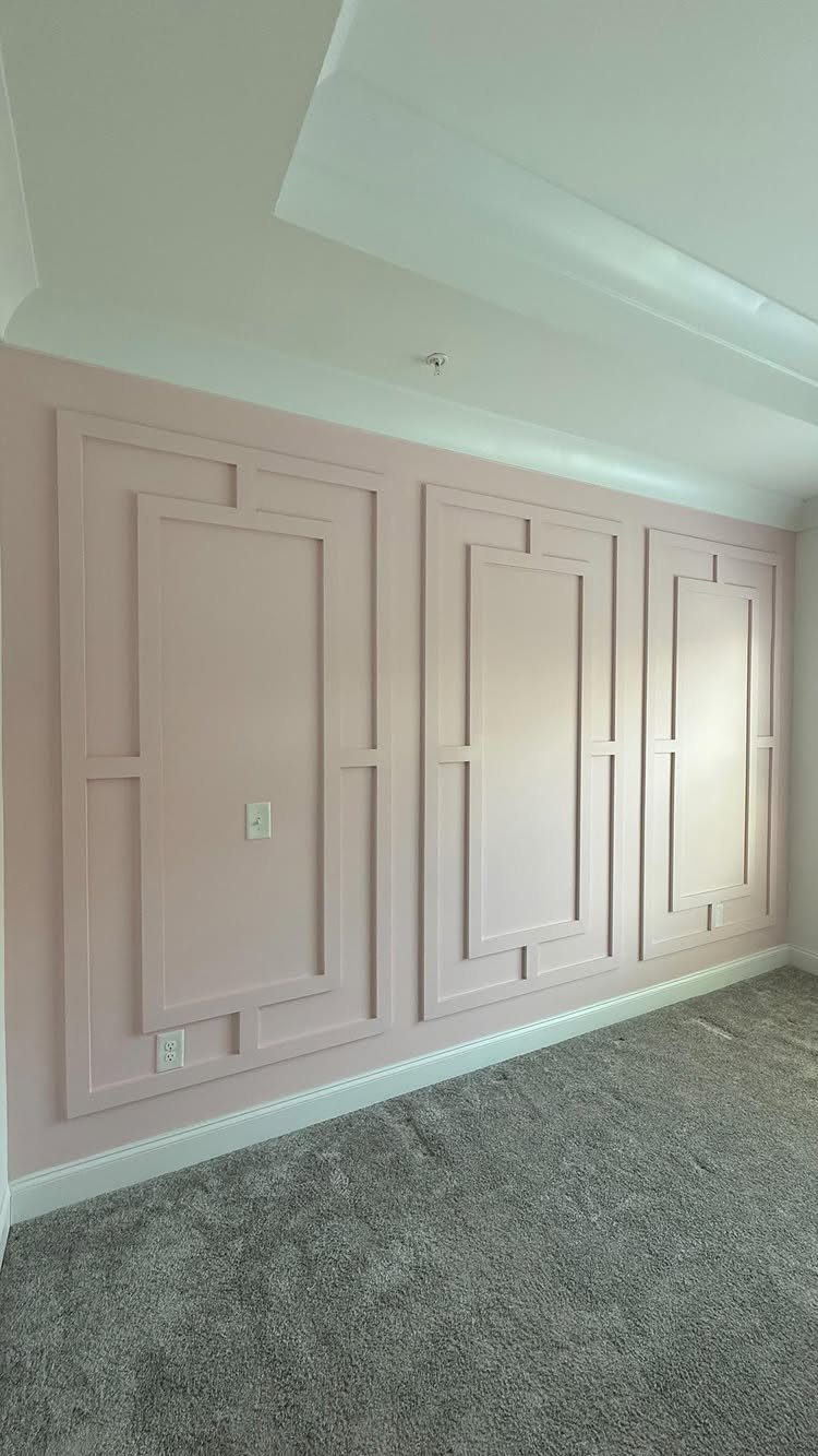 Light pink wall with decorative board and batten molding panels and grey carpet.