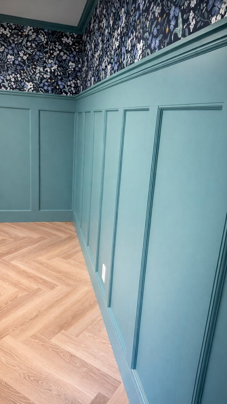 Teal board and batten wainscoting wall with floral wallpaper and herringbone wood floors.