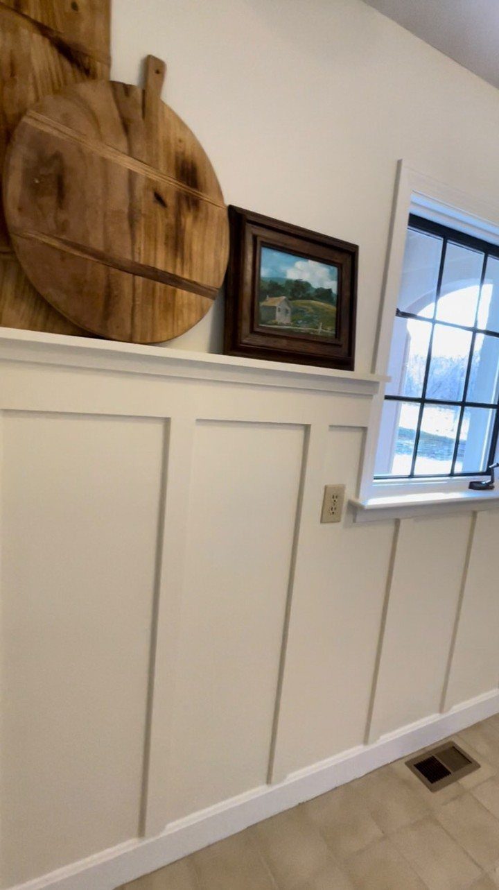 White board and batten wall with a ledge holding wooden decor and art.