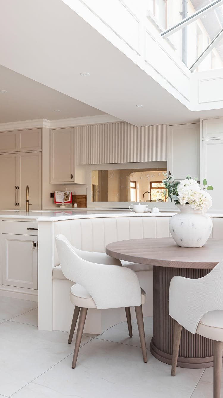 White built-in dining banquette with a round wooden pedestal table and white chairs.