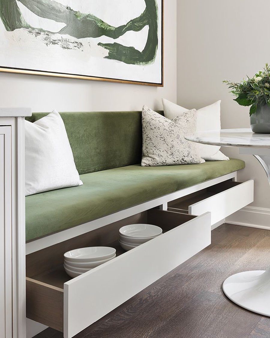 Green velvet built-in dining bench with white storage drawers and marble table.
