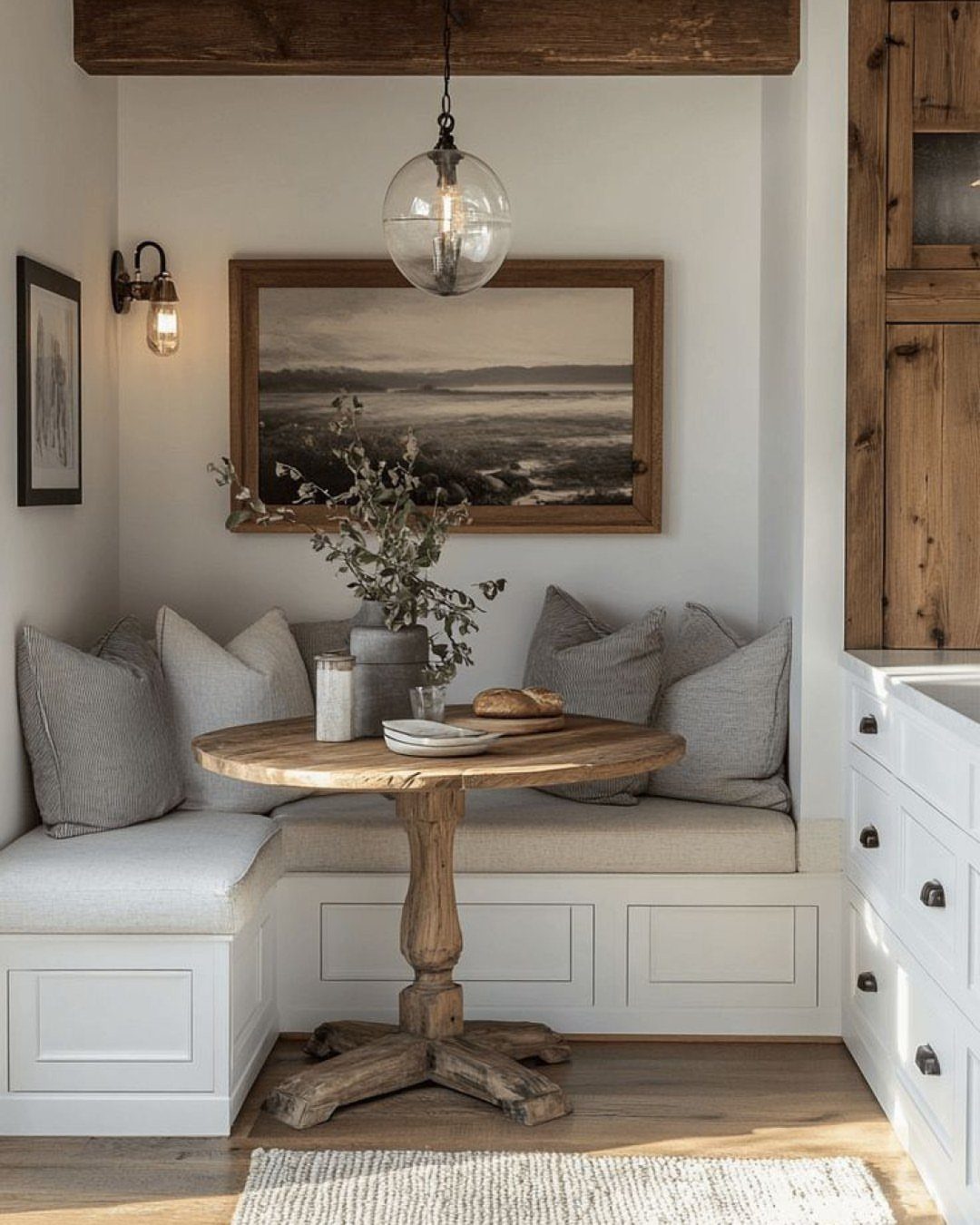 White L-shaped built-in dining bench with grey cushions and a wooden pedestal table.