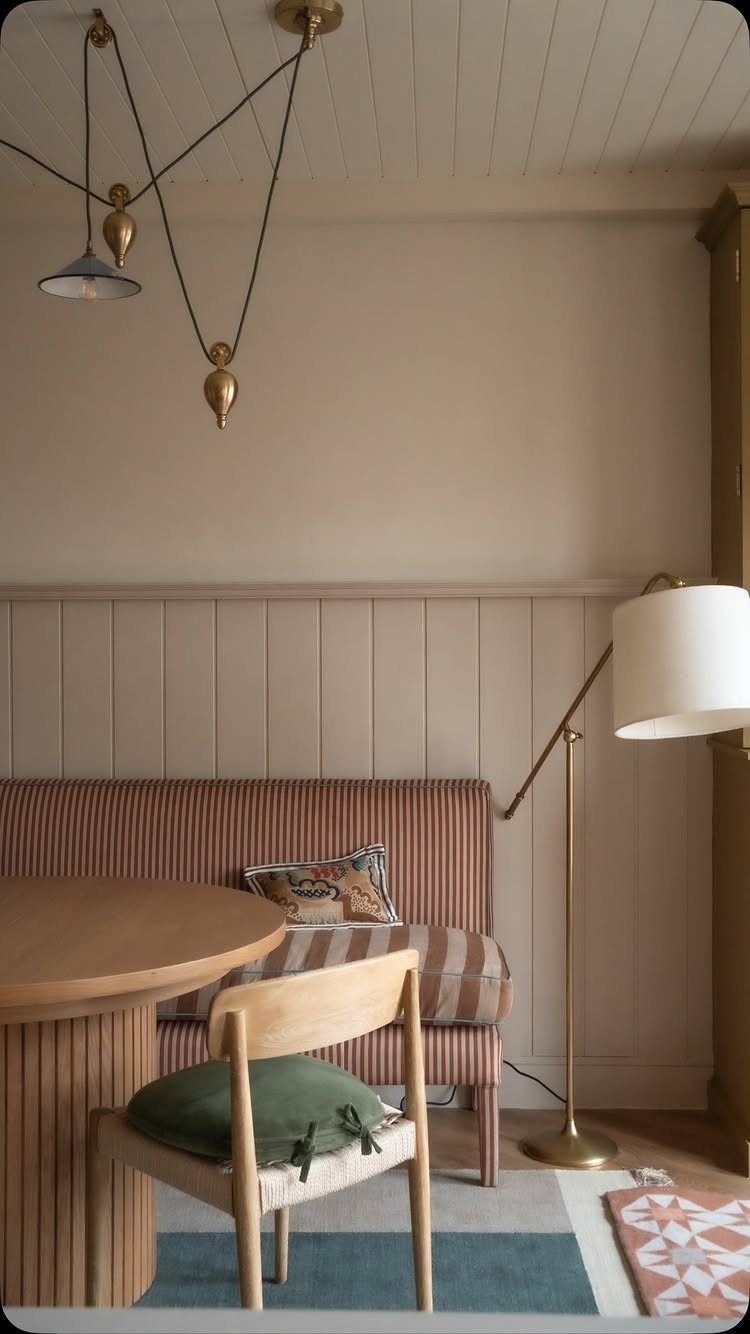 Built-in striped dining bench with a round wooden table and gold floor lamp.