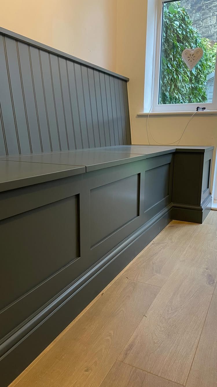 Grey built-in dining bench with paneled base and slat backrest on wood floor