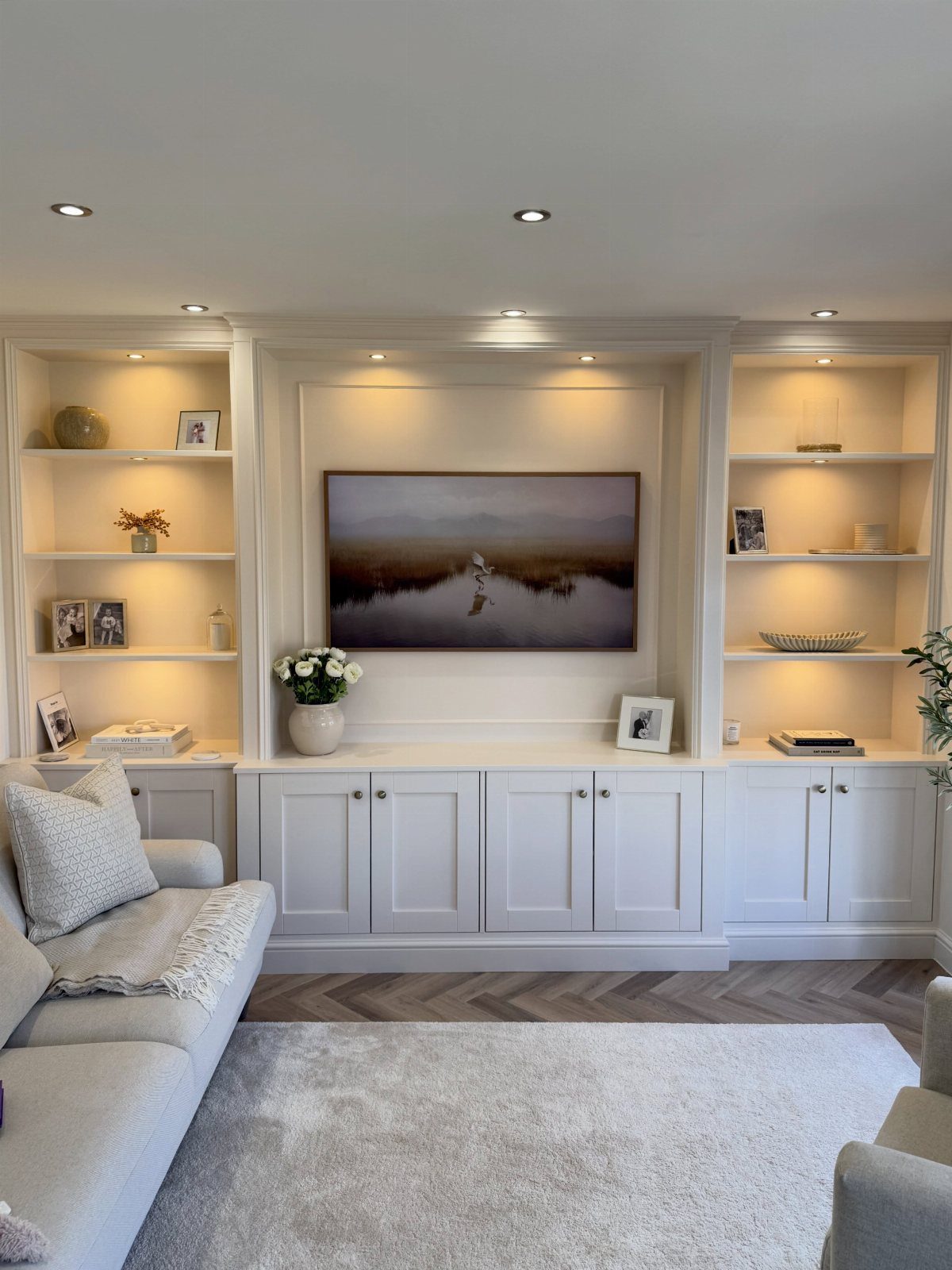 White built-in entertainment center with recessed television, open shelving, and integrated warm lighting.