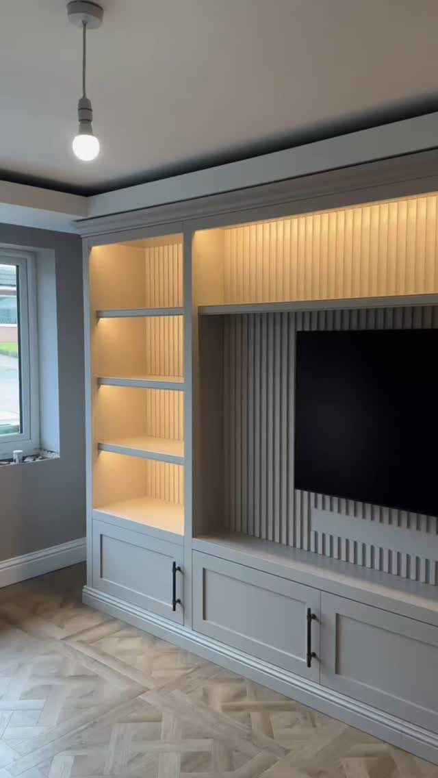 Light grey built-in entertainment center with open lit shelves and closed bottom cabinets.