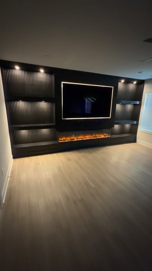 Black custom entertainment center with integrated lighting, television, and linear electric fireplace.