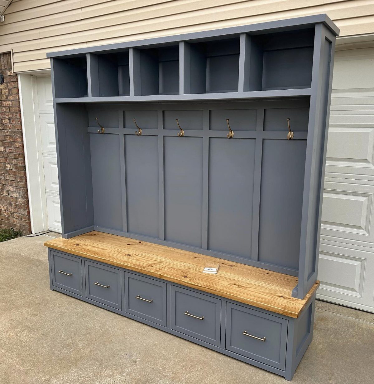 Grey built-in hall tree with natural wood bench and storage drawers outdoors.
