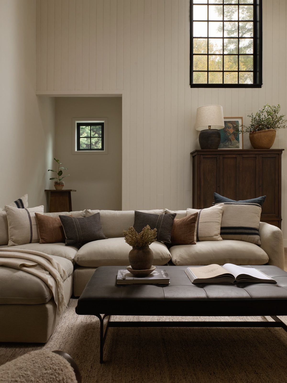 Cream sectional sofa with layered linen pillows and a black leather ottoman coffee table.